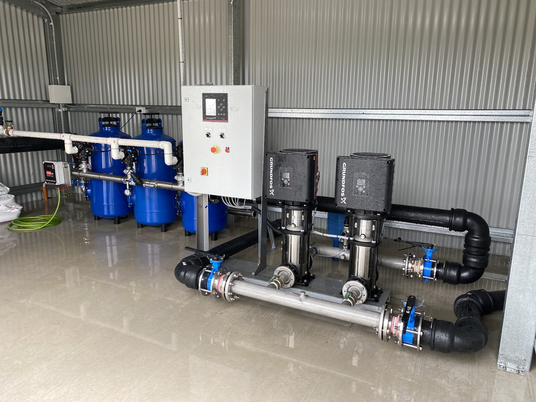 Twin Grundfos pumps, blue filter vessels and a control panel in a shed pump room